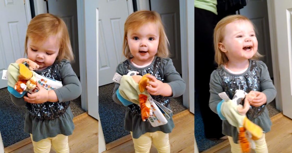 A toddler in an indoor setting, wearing a dark green long-sleeved shirt with sequins and light yellow pants. The background includes white doors and a dark blue carpeted area.