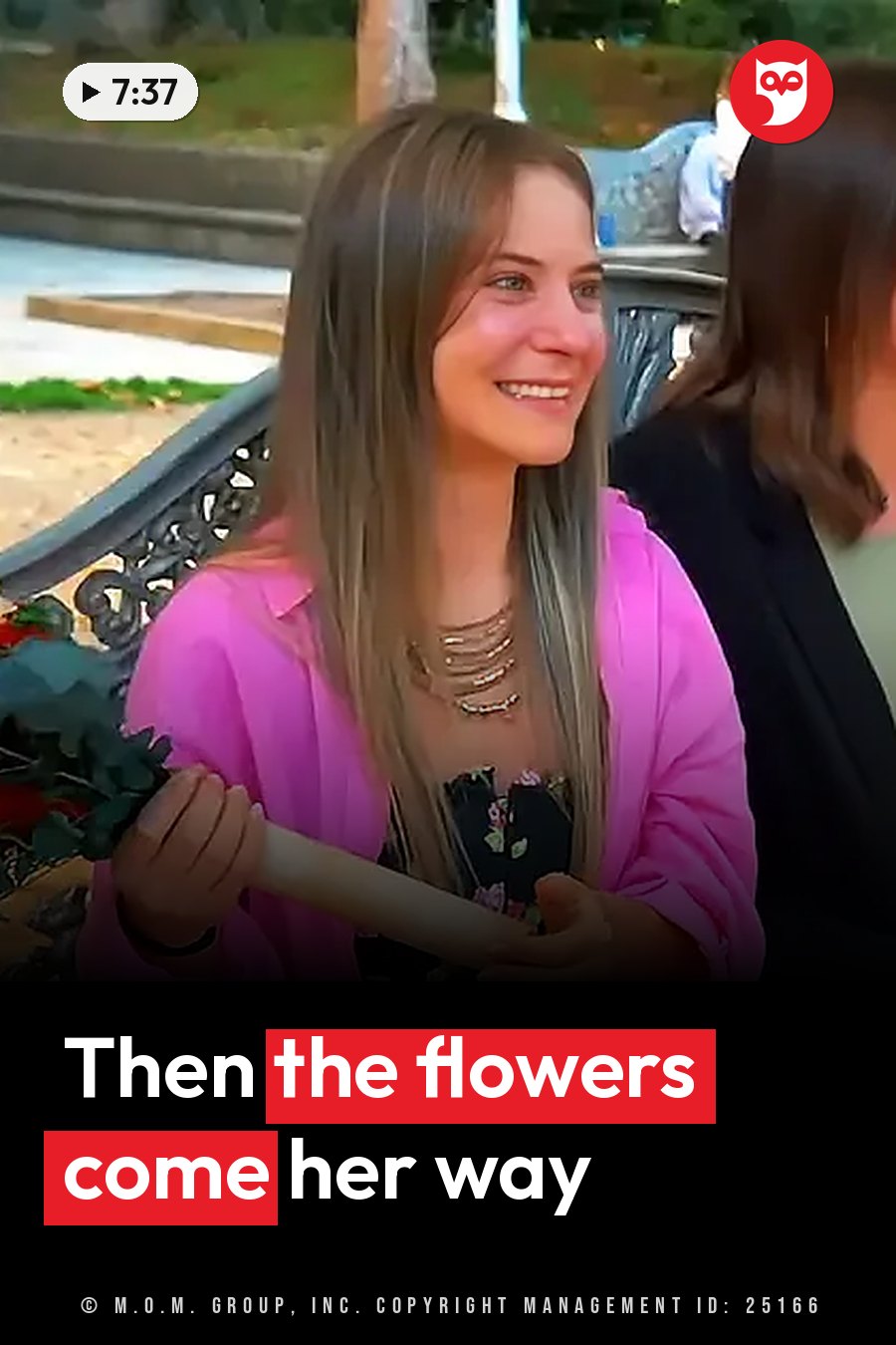 A woman with long hair smiles, holding flowers, sitting outdoors near a decorative bench. A headline runs in white letters across the lower third.