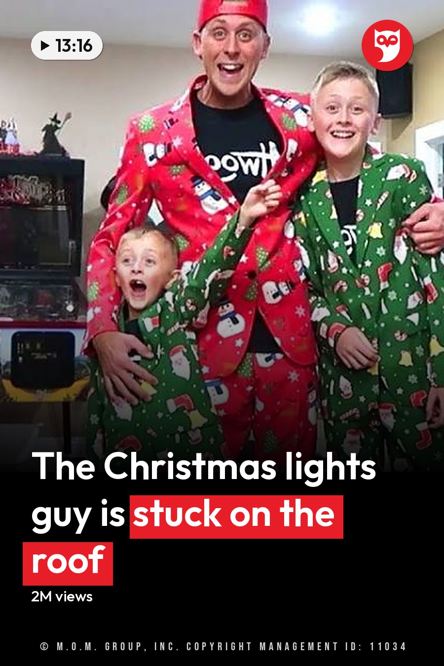 Adult Female carrying clothes, wearing light gray top and black pants with rips; Adult Male in red Santa suit jacket over t-shirt and green pajama-style pants; Child in green Santa-themed pajama set standing near adult male; Teen/Young Adult Male in similar attire to the adult male. Scene includes dark brown couch, arcade machine, television showing colorful display, plastic storage bins, baby swing with toys attached. The headline runs in white letters across the lower third.