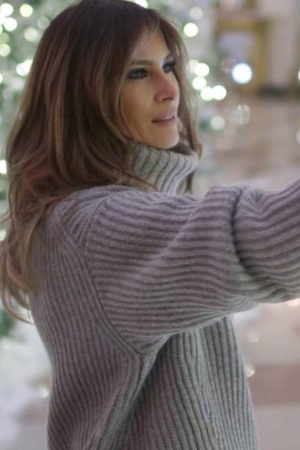 A middle-aged female in a festive indoor setting, decorated for Christmas with white lights and icicle ornaments on a tree.