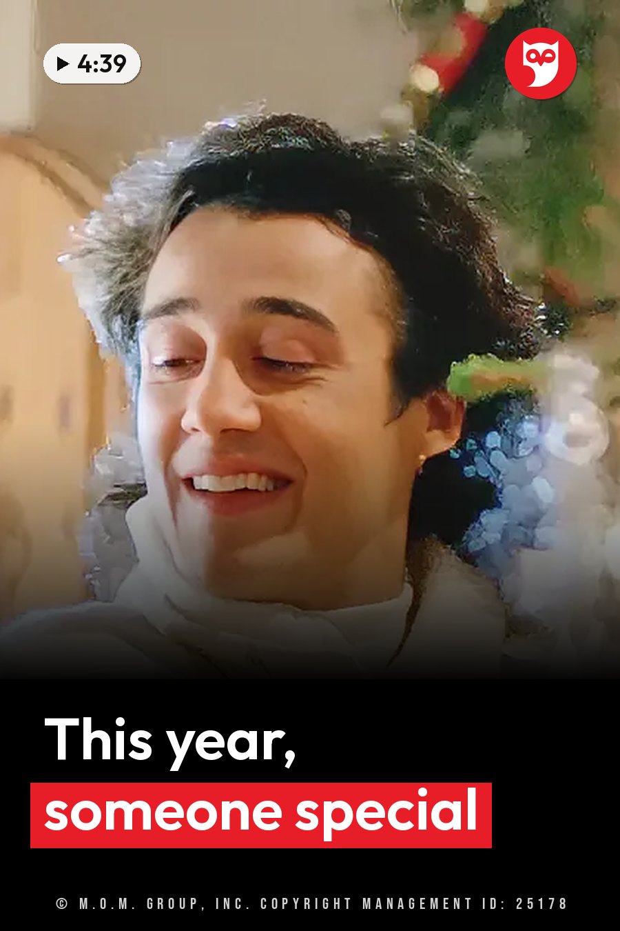 A man with dark hair in a white high-necked top smiles softly near a decorated Christmas tree. A headline runs in white letters across the lower third.