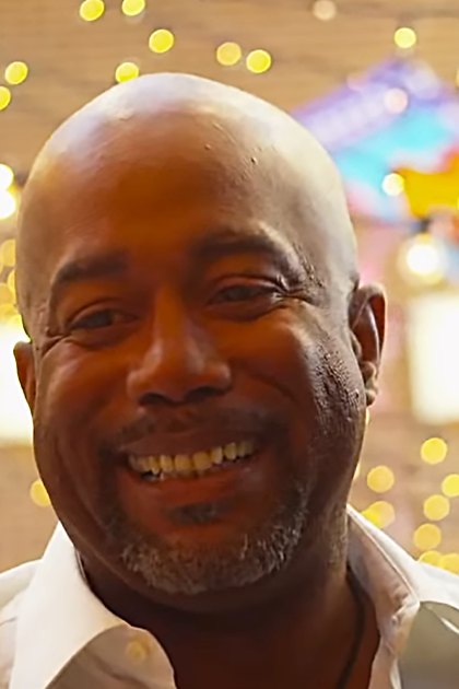 An older adult male wearing a white collared shirt in a festive indoor setting with string lights and decorations.