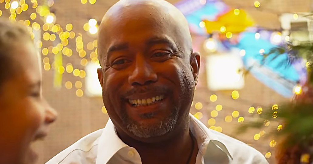 An older adult male wearing a white collared shirt in a festive indoor setting with string lights and decorations.