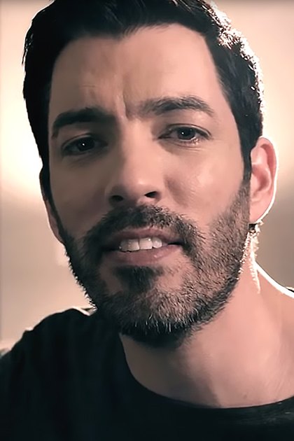 A young adult male in a relaxed fit crew neck t-shirt with short sleeves, wearing modern casual wear indoors with soft lighting and warm tones dominating the background.