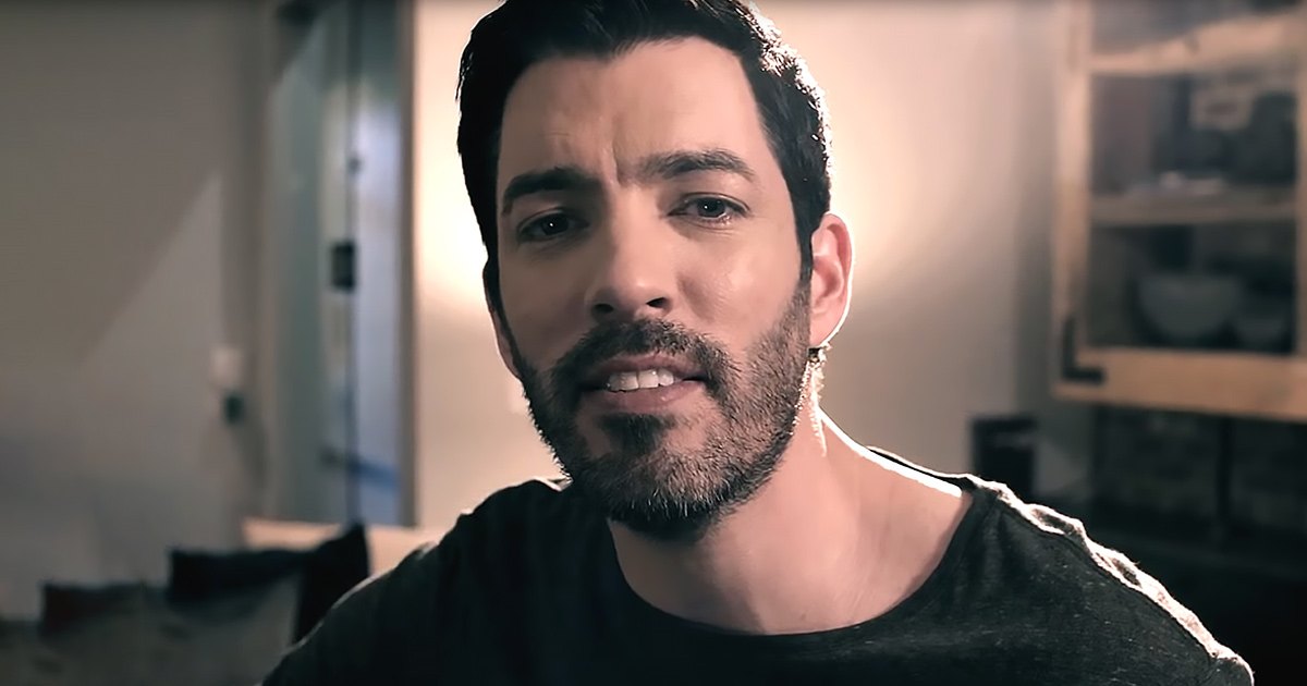 A young adult male in a relaxed fit crew neck t-shirt with short sleeves, wearing modern casual wear indoors with soft lighting and warm tones dominating the background.