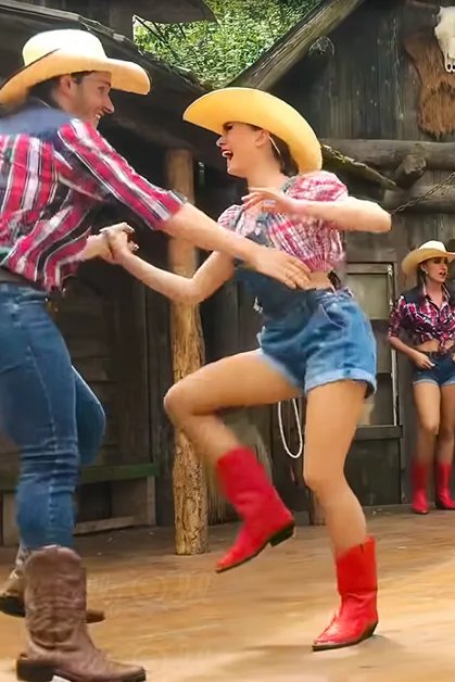 A group dancing in a rustic setting, likely at an amusement park or themed attraction.